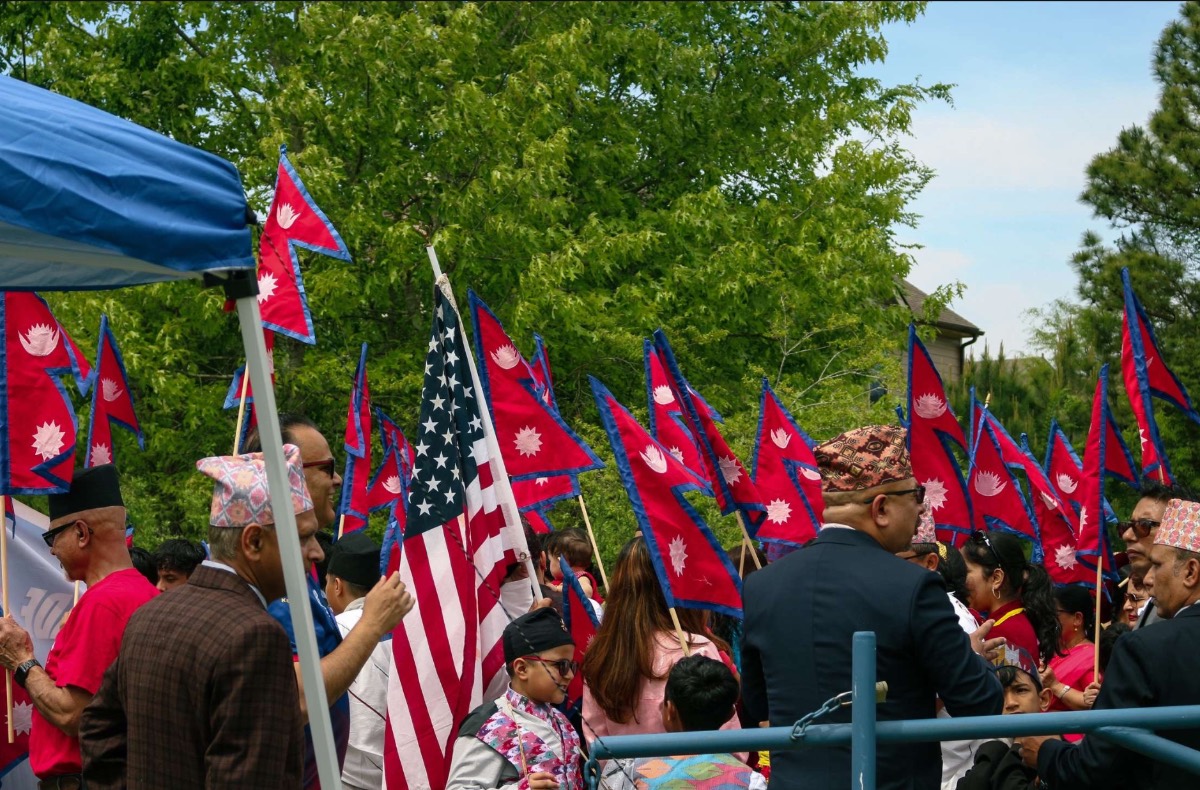 A crowd waving Nepali and American flags together under the trees