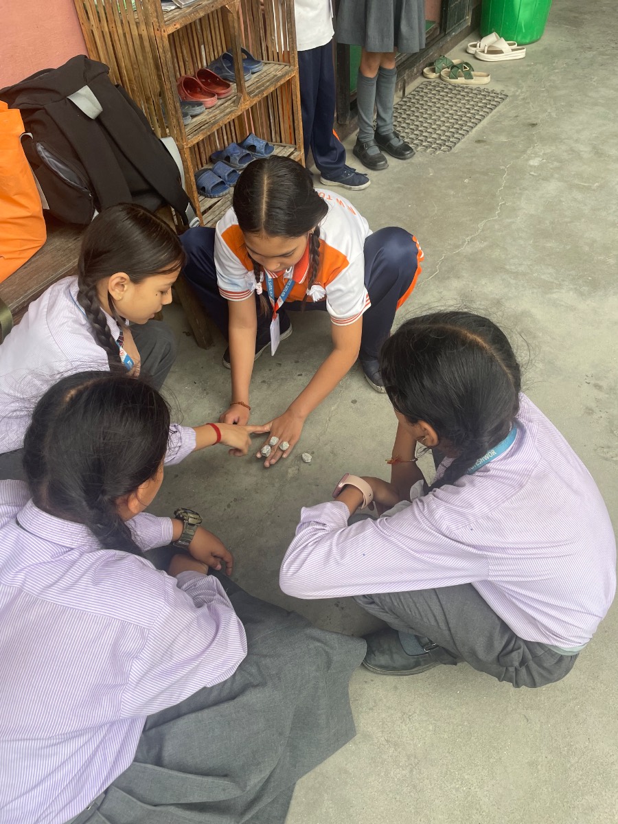 Schoolgirls in uniform crouched in a circle playing a game of stones