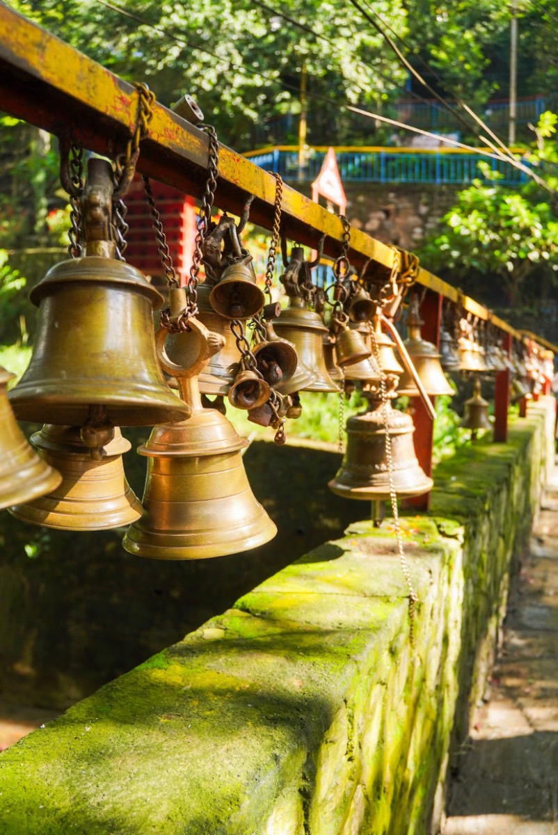 A row of brass bells hanging along a mossy temple wall